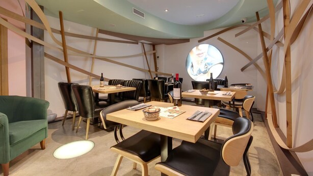 Un interior de restaurante con mesas redondas, sillas de cuero negro y un sofá verde.