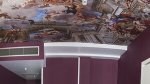 Un dormitorio con un gran mural en el techo que representa una escena clásica con figuras y nubes.