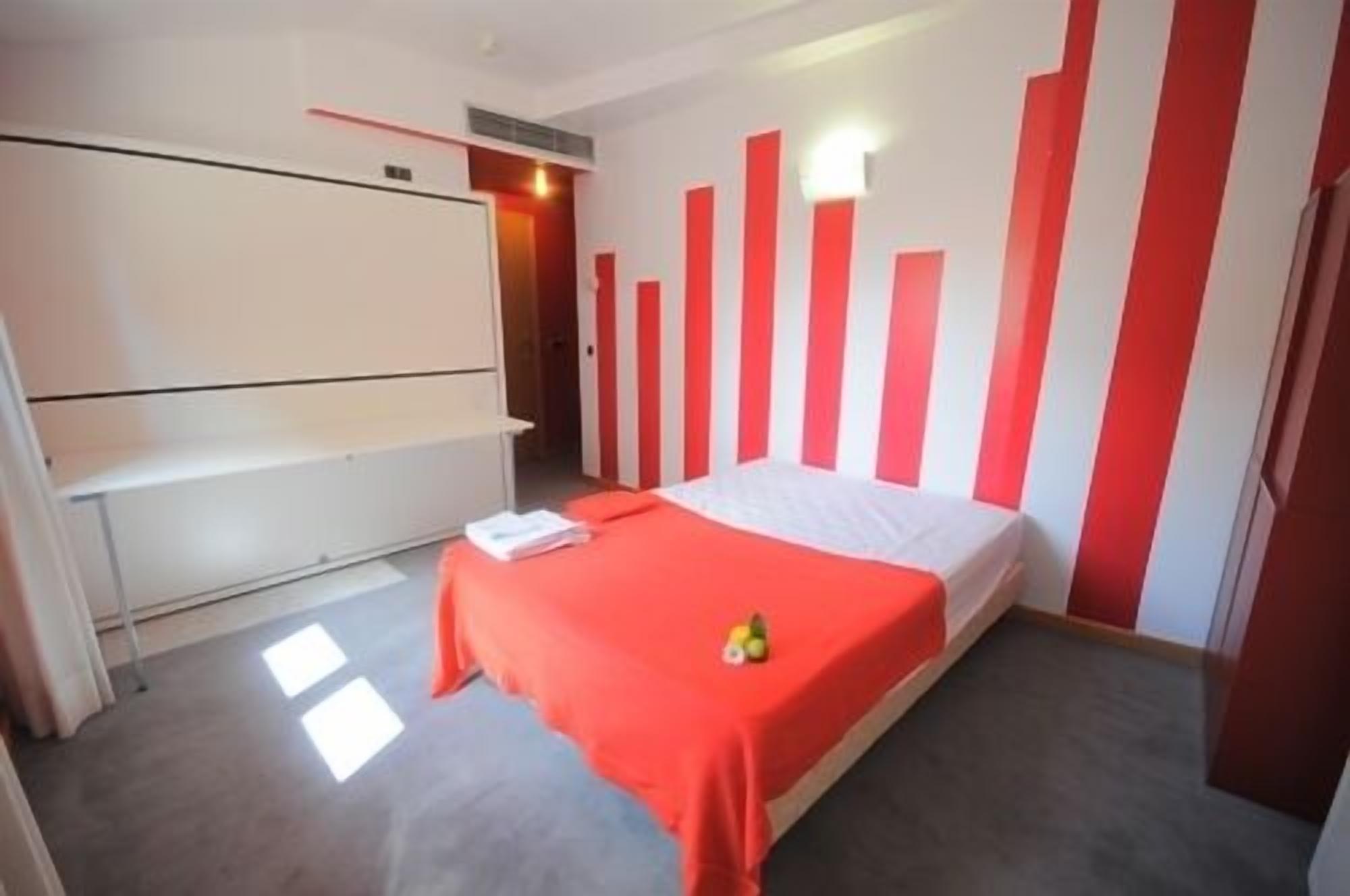 Una habitación con una cama, un armario blanco y una pared con rayas verticales rojas y blancas.