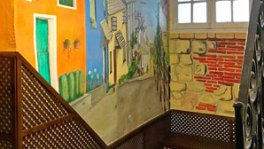 A mural of a colorful street scene on a staircase wall, featuring a blue building with a green door and a yellow building with a brick facade. - Sweet Home (Salamanca)