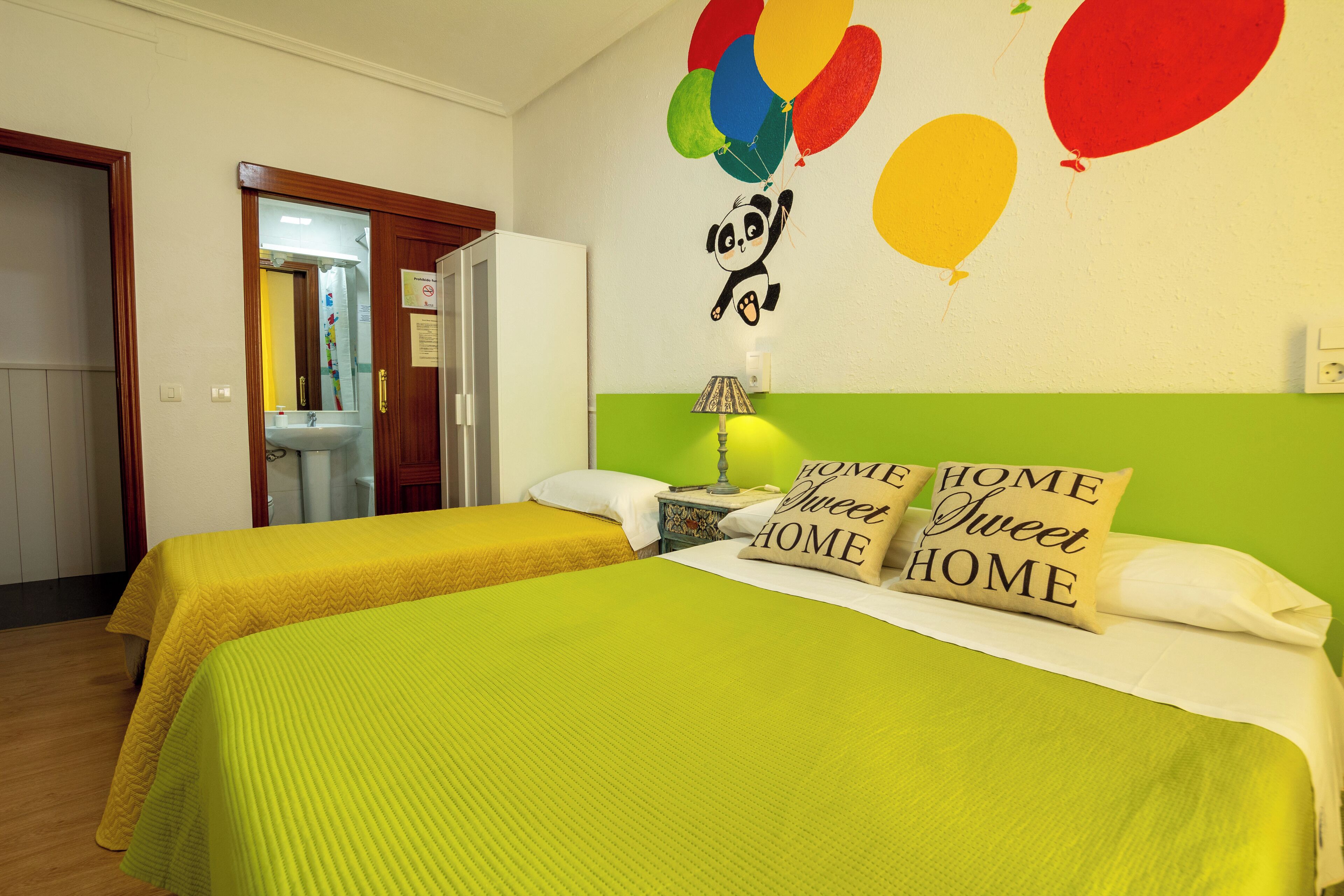 Una habitación con dos camas, una pared verde y una decoración de panda con globos.