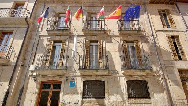 A historic building with multiple balconies, flags, and a bicycle parked in front. - Sweet Home (Salamanca)