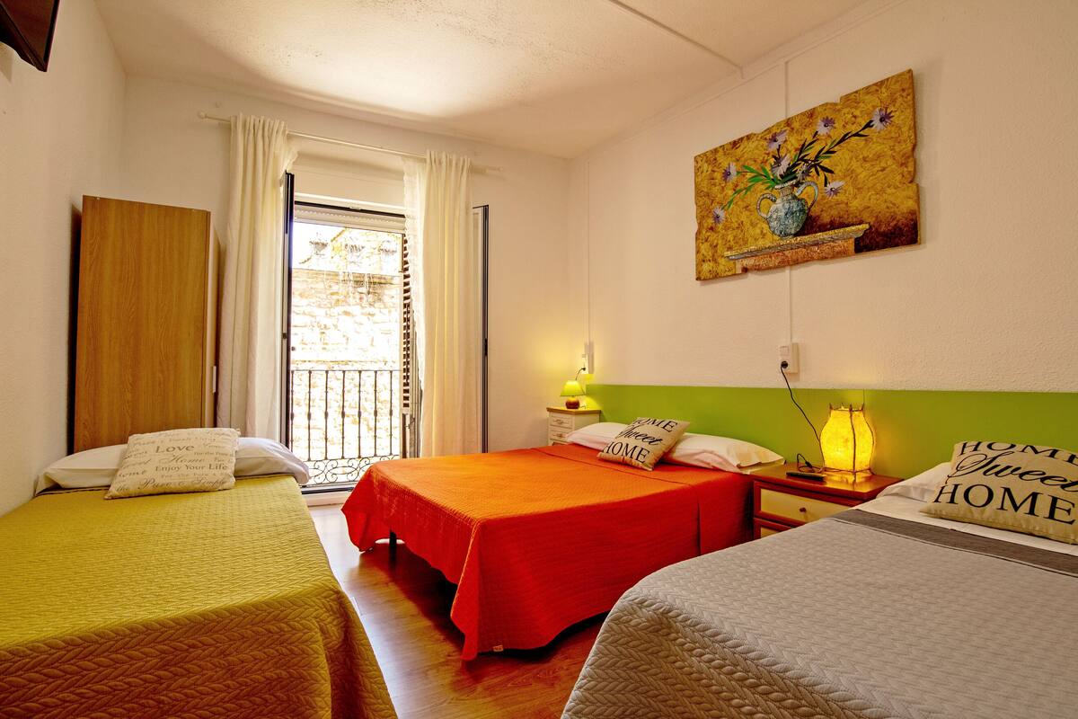 A hotel room with two single beds, a nightstand with a lamp, a painting on the wall, and a window with curtains.