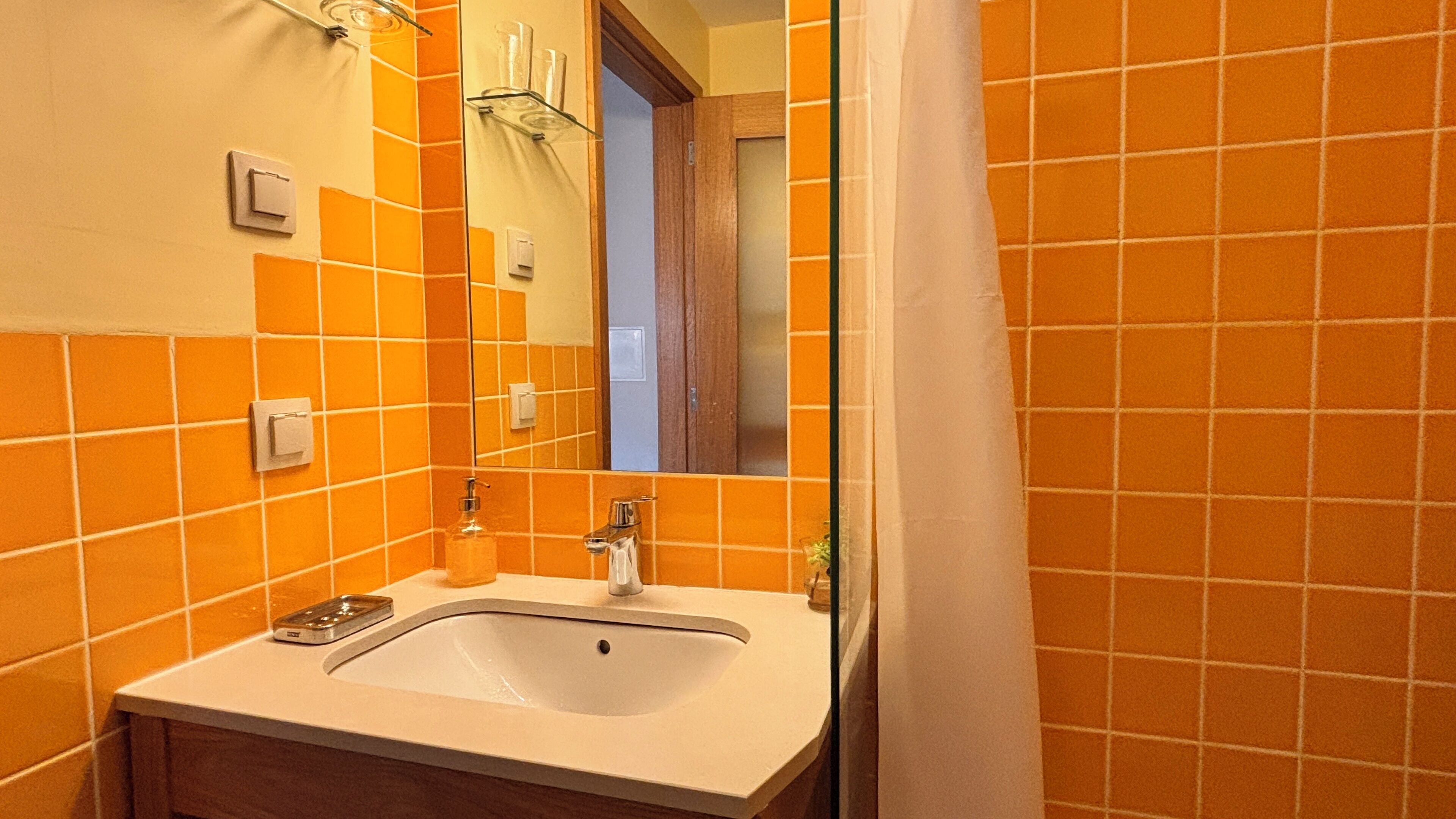 Un baño con paredes de azulejos naranjas, un lavabo blanco y un espejo.