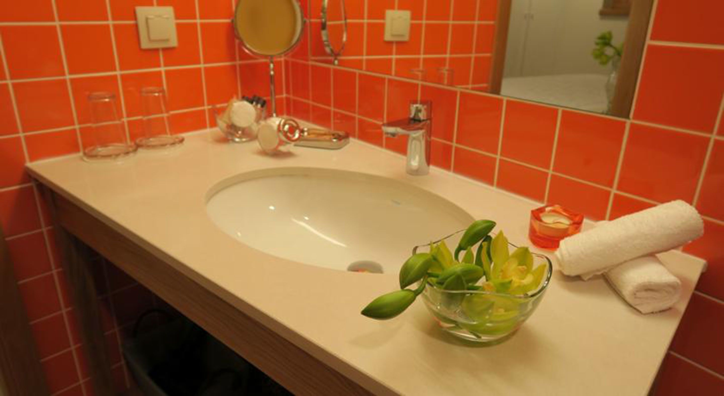 A bathroom with a white sink, a mirror, and a glass bowl with green leaves.