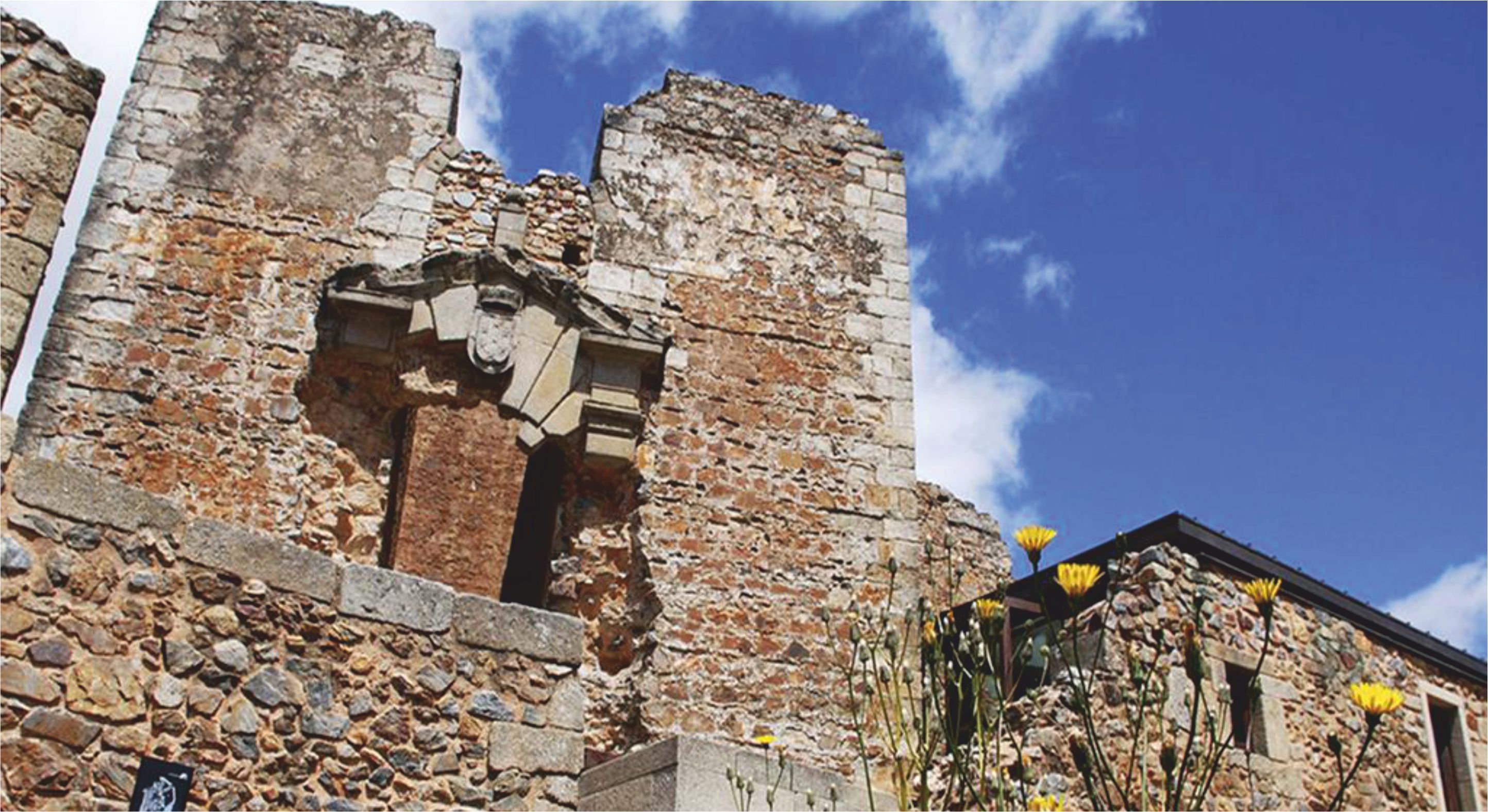 A historic stone building with visible structural damage and a clear sky.