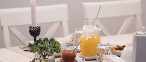 A table set with a candle, a glass of orange juice, a small dish of jam, and a glass of water.