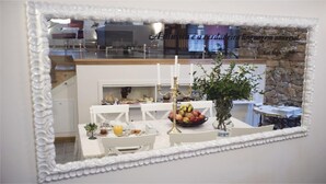 Un comedor con una mesa blanca dispuesta para dos personas, un frutero y un florero con flores.