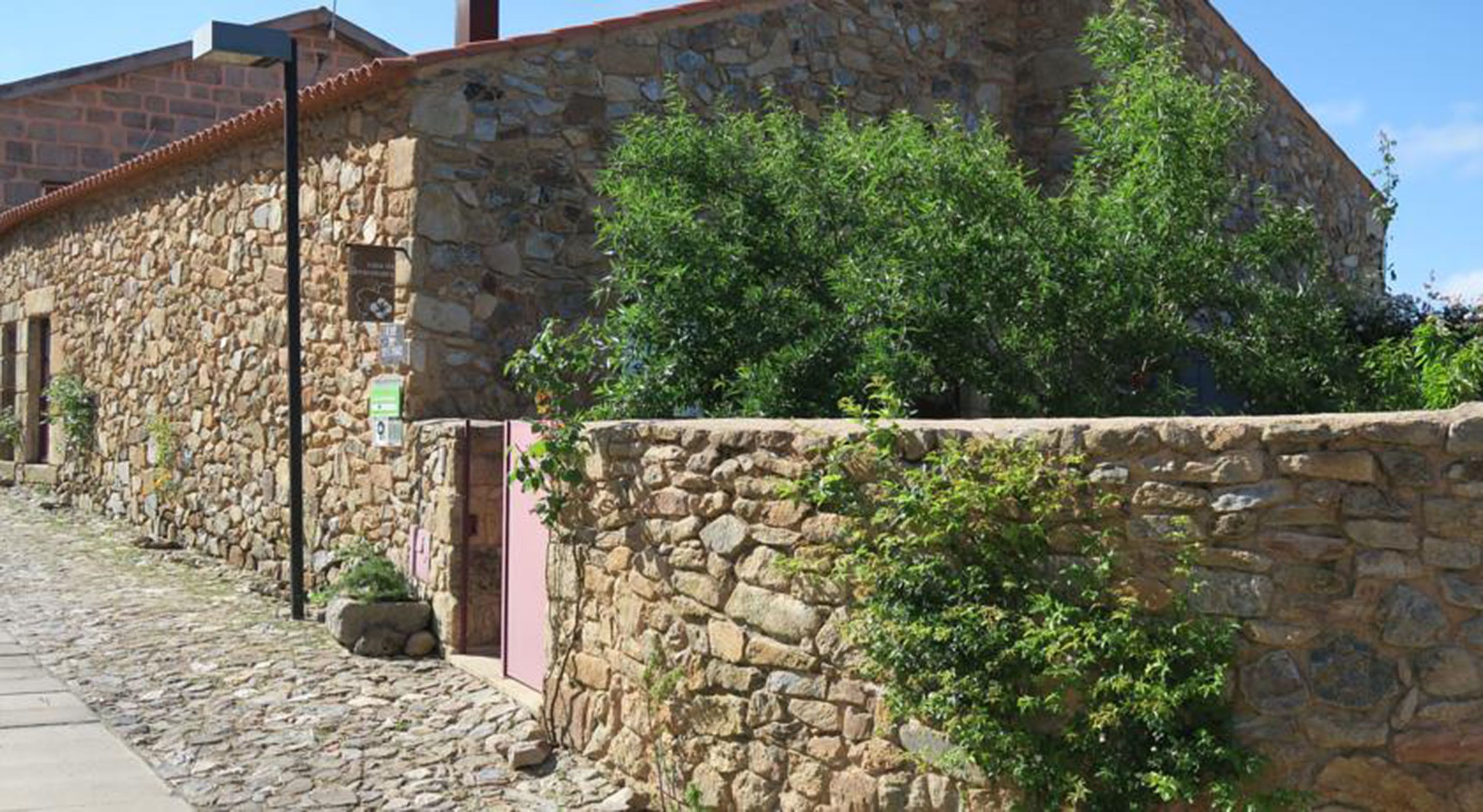 A stone building with a tiled roof, a paved pathway, and a stone wall with greenery.