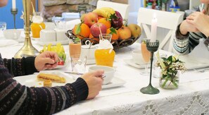 Una escena de desayuno con un bol de fruta, zumo de naranja y una vela sobre una mesa.