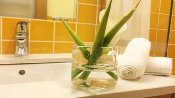 Un lavamanos con un jarrón de vidrio que contiene hojas de aloe vera y una toalla blanca enrollada a un lado.