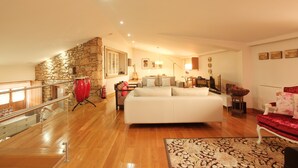 Amplia sala de estar con una cama grande, pared de piedra, batería roja y barandilla de cristal.