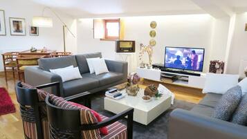 Una sala de estar moderna con un sofá gris, una mesa de centro con objetos decorativos, un televisor y un comedor con mesa y sillas de madera.