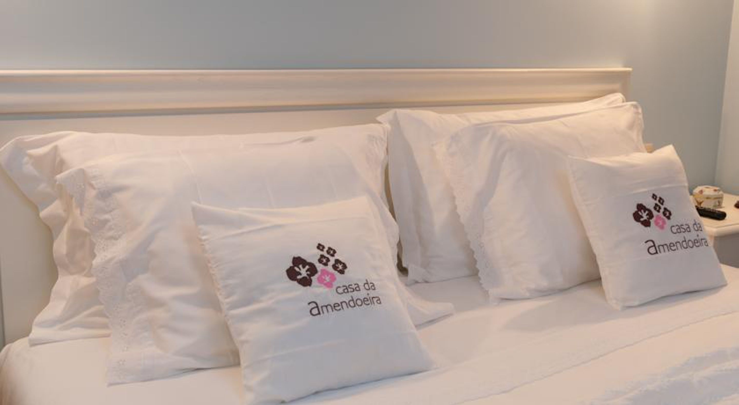 Una cama con ropa blanca y almohadas, cada una con el logo y el texto 'casa da amendoeira'.