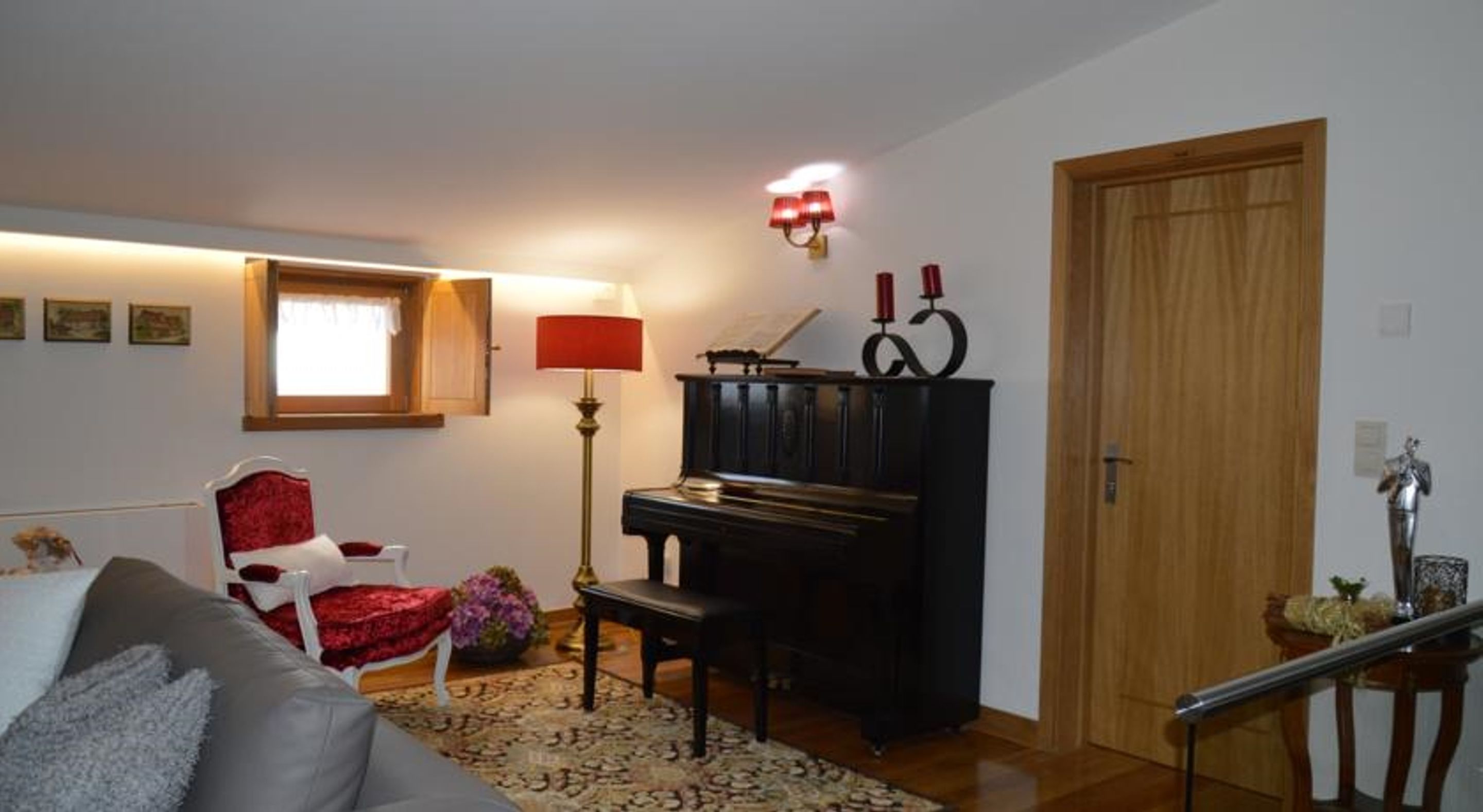 A living room with a piano, a red armchair, a sofa, and a lamp.