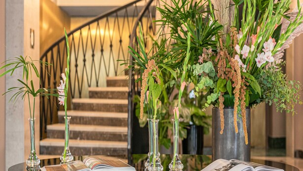Una escalera con barandilla de metal, rodeada de plantas en macetas y jarrones con flores.