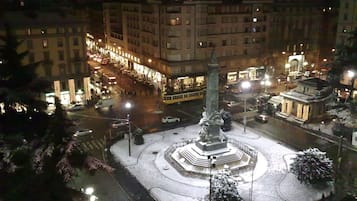 Vista nocturna de una plaza urbana con un monumento central, edificios circundantes y una calle concurrida con vehículos.