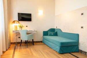 Et værelse med en turkis sofa, et skrivebord med lampe, et fjernsyn monteret på væggen og en lille plante på skrivebordet.