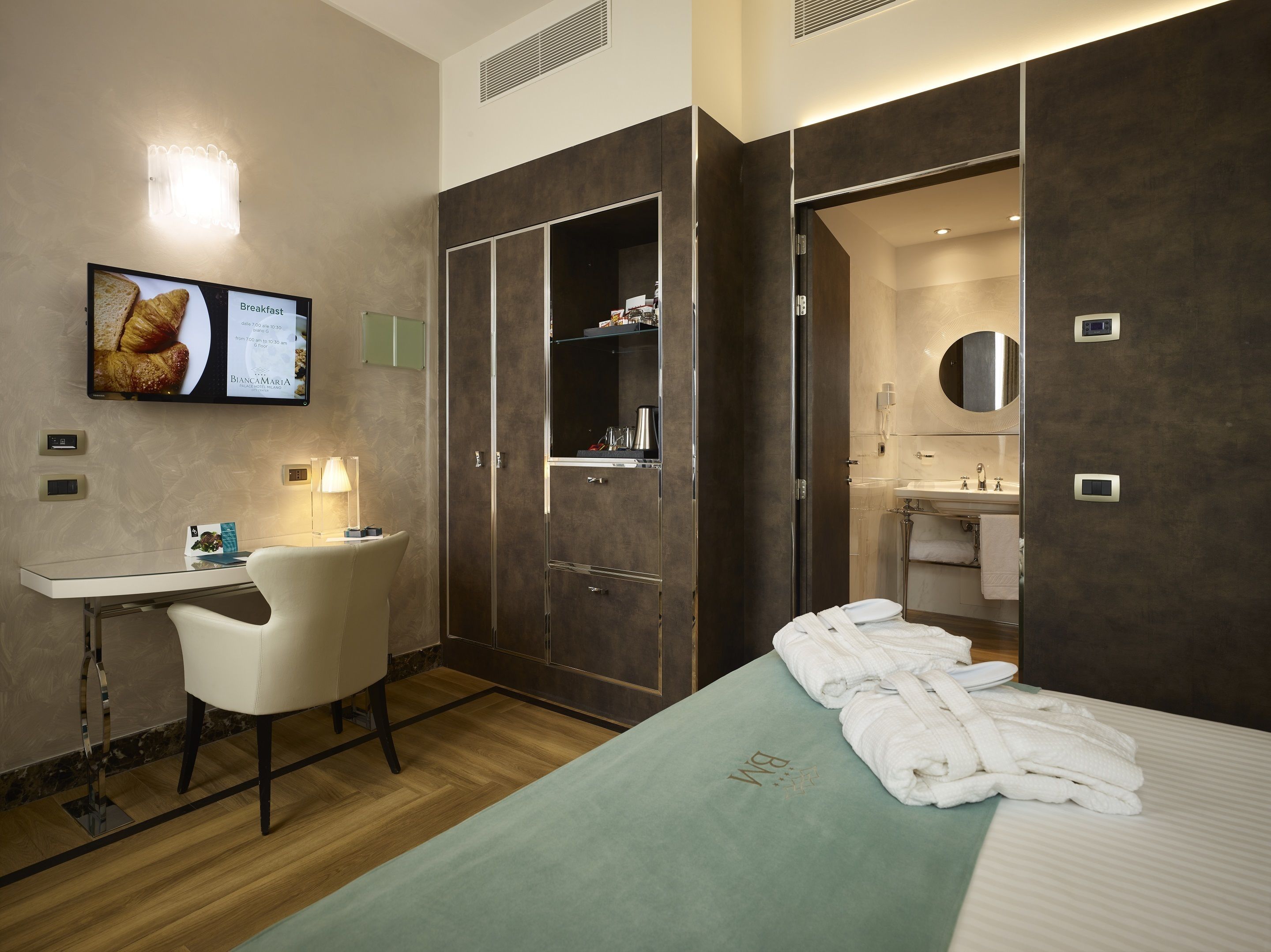 Una habitación de hotel con cama, escritorio, silla, televisión y baño.