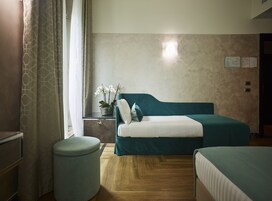 A hotel room with a bed, a bedside table with a lamp, a small potted plant, and a wall-mounted light fixture.