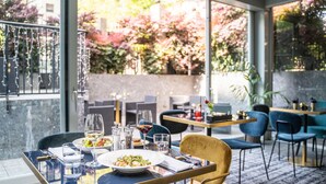 Un restaurante con mesa y sillas de vidrio, un plato de comida, copas de vino y un salero y pimentero.