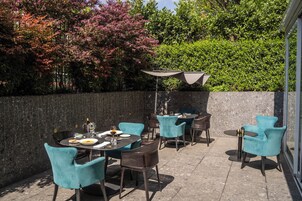 Patio esterno con tavoli e sedie, circondato da un muro in pietra e vegetazione lussureggiante.