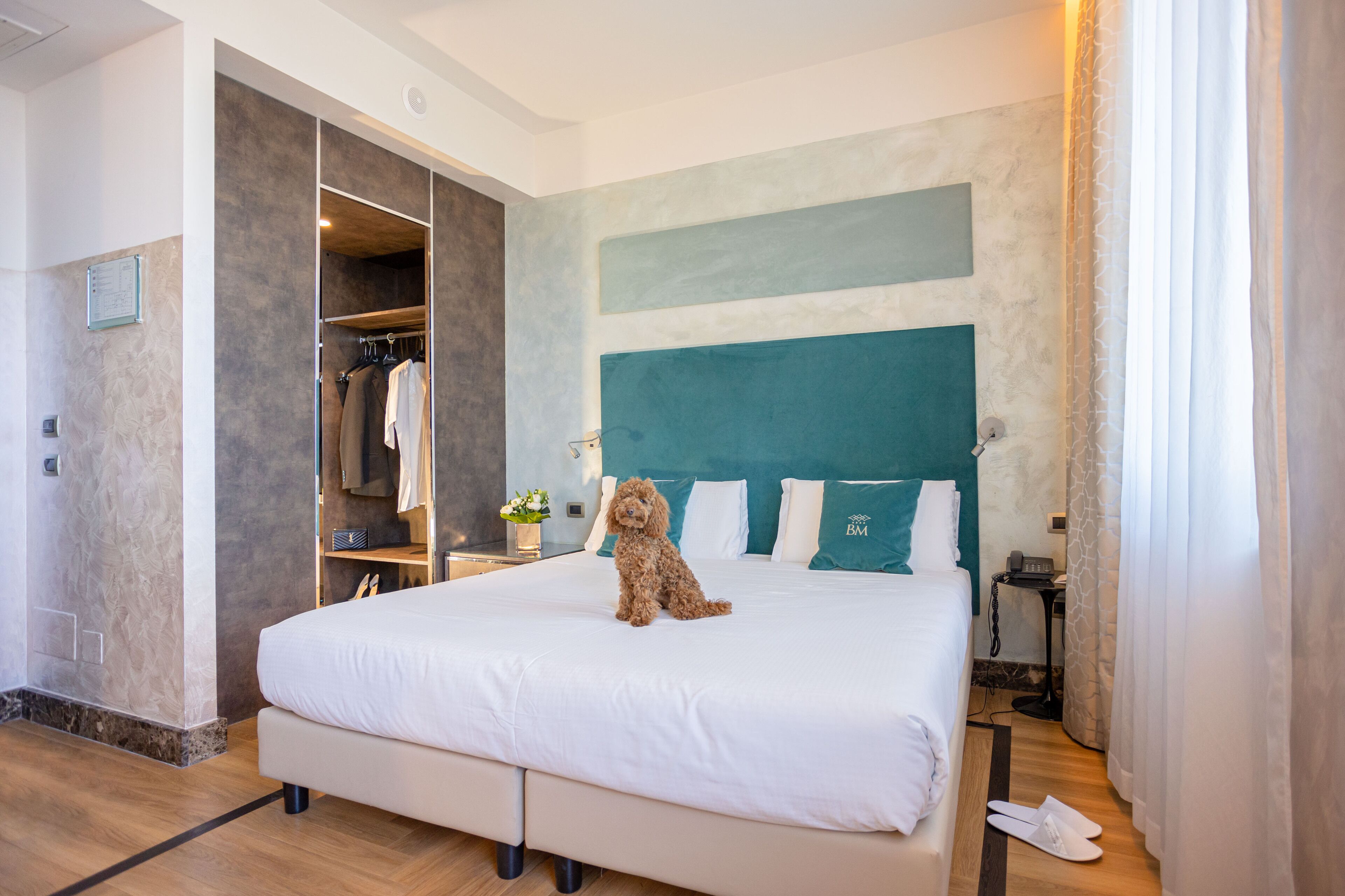 A hotel room with a large bed, a built-in wardrobe, a small table with a vase of flowers, and a view of the city.