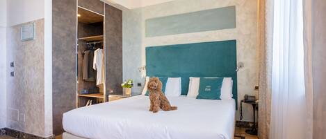 A hotel room with a large bed, a built-in wardrobe, a small table with a vase of flowers, and a view of the city.