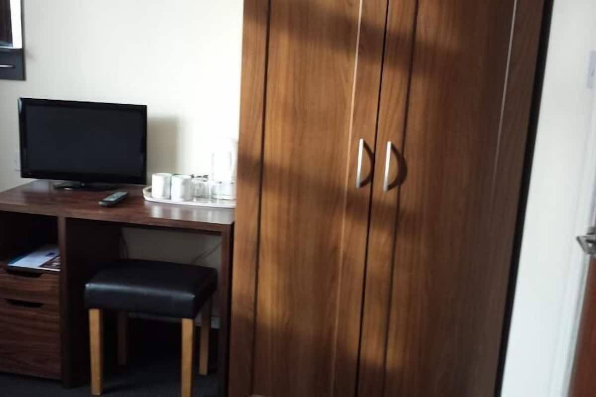 A room with a wooden desk, a television, a small stool, and a wardrobe with two doors.