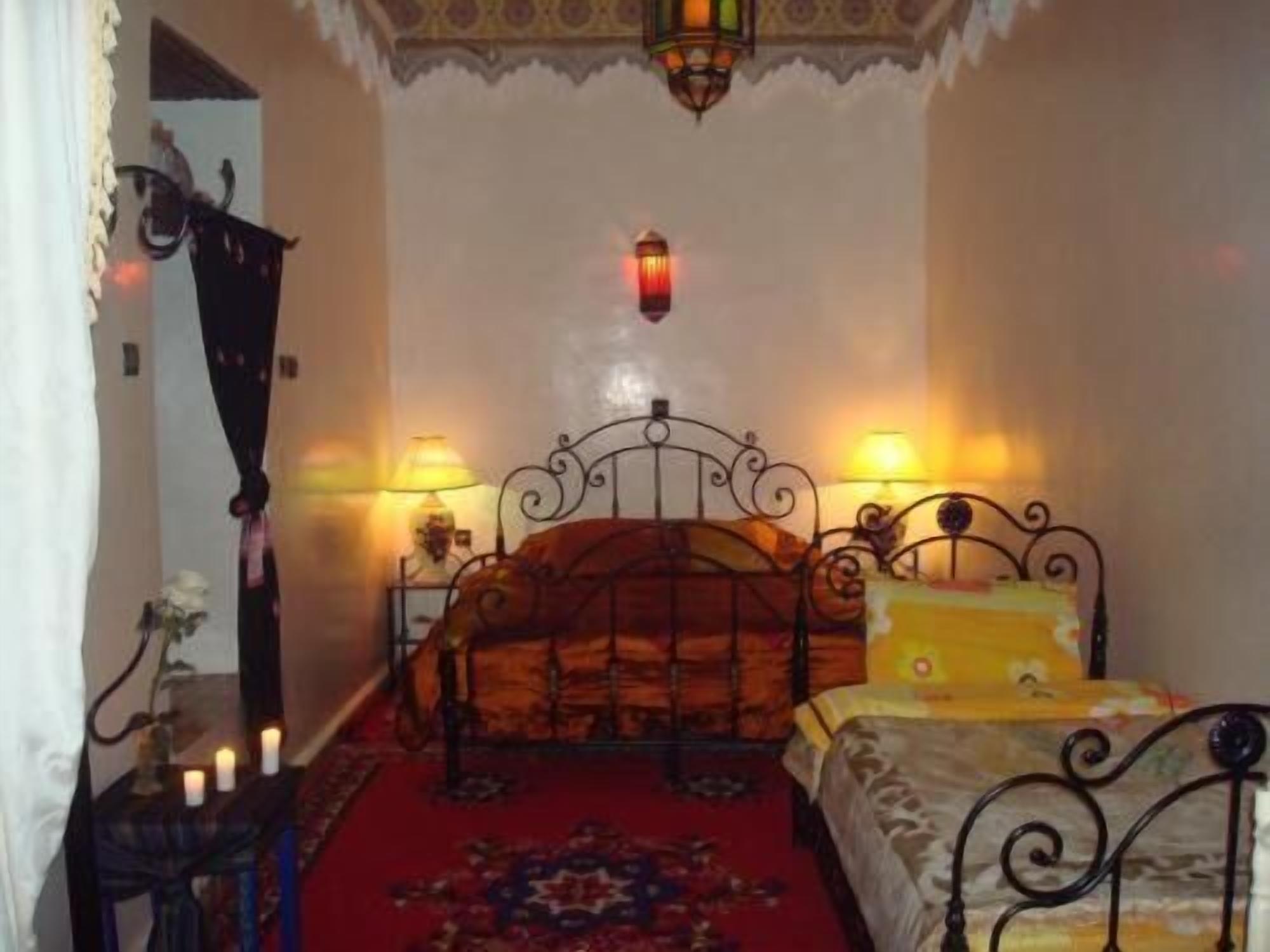 Un dormitorio con cama, dos lámparas de noche, una mesita de noche con lámpara, un tapete estampado y un adorno en la pared.
