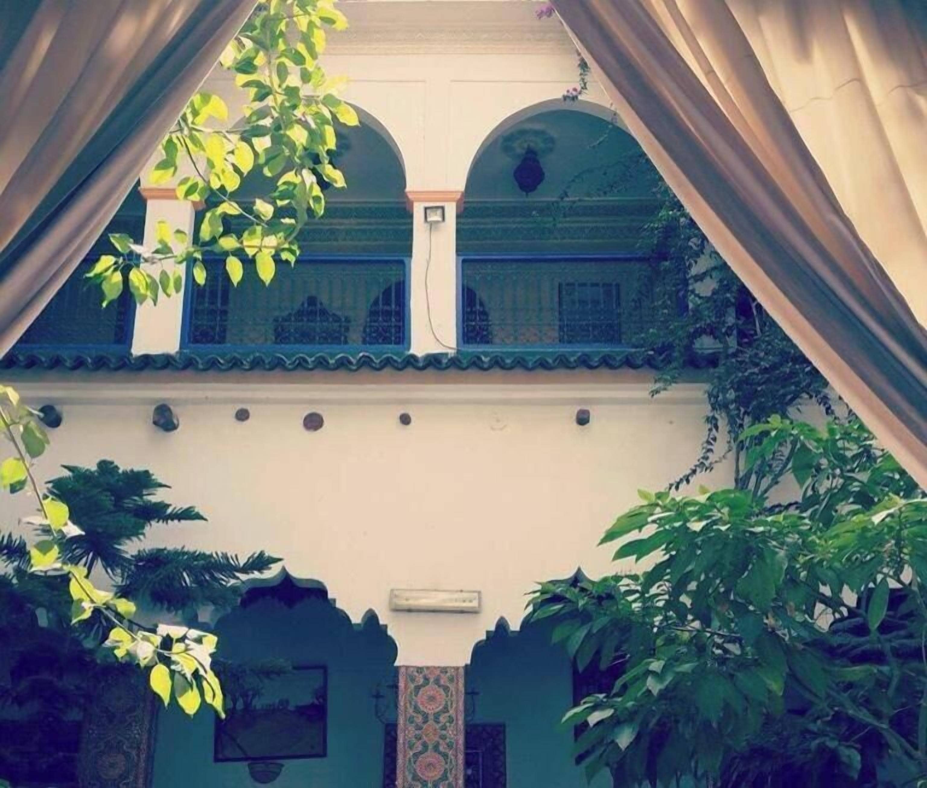 A courtyard with a balcony, a white wall, and a patterned door.