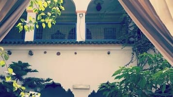 A courtyard with a balcony, a white wall, and a patterned door.