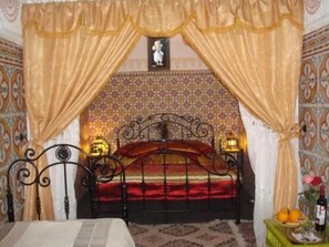 A bedroom with a bed, curtains, a nightstand with a lamp, and a wall with a patterned design.
