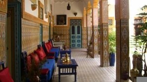 A corridor with a blue sofa, a table with a golden object, and a door with geometric patterns. - Riad Maryam (Taroudant)