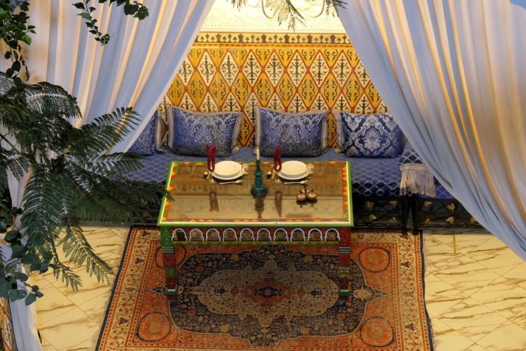 A room with a patterned sofa, a table with a patterned tablecloth, and a decorative rug.