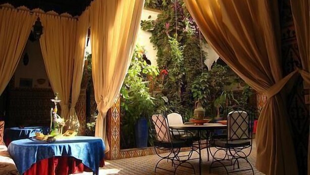 A dining area with a table and chairs, surrounded by curtains and plants. - Riad Maryam (Taroudant)