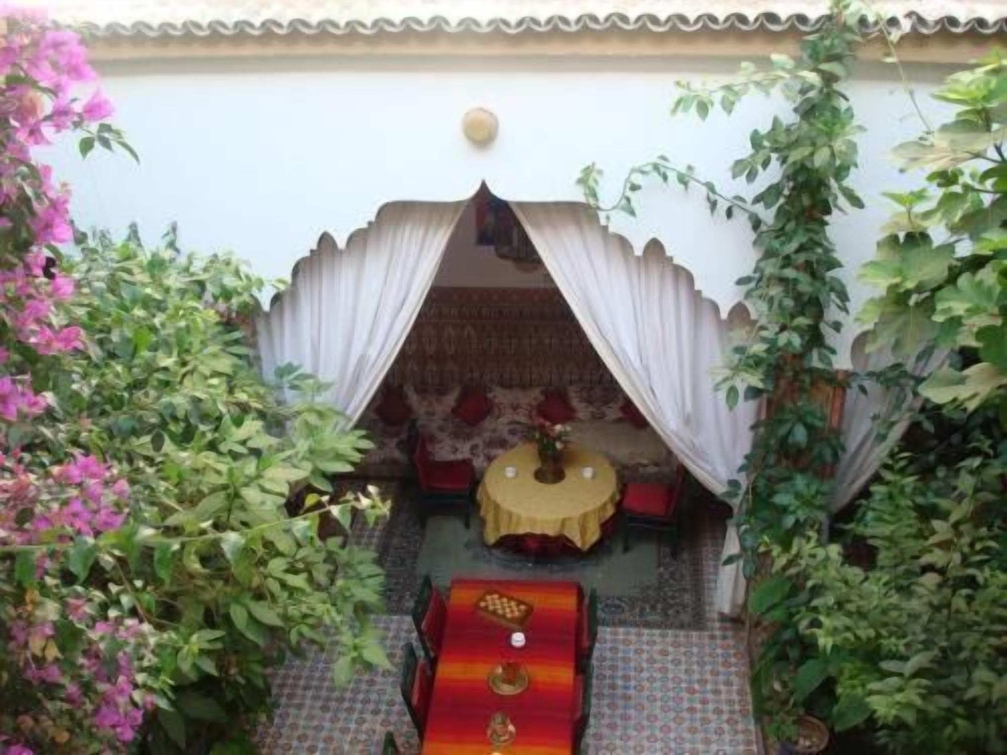 A traditional room with a patterned carpet, a bed with a red and gold headboard, and a small table with a yellow tablecloth.