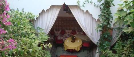 A traditional room with a patterned carpet, a bed with a red and gold headboard, and a small table with a yellow tablecloth.
