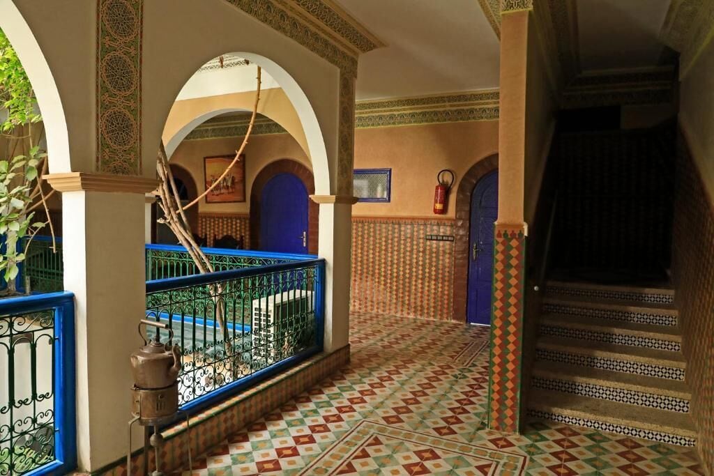 A corridor with patterned flooring, blue doors, and decorative arches.