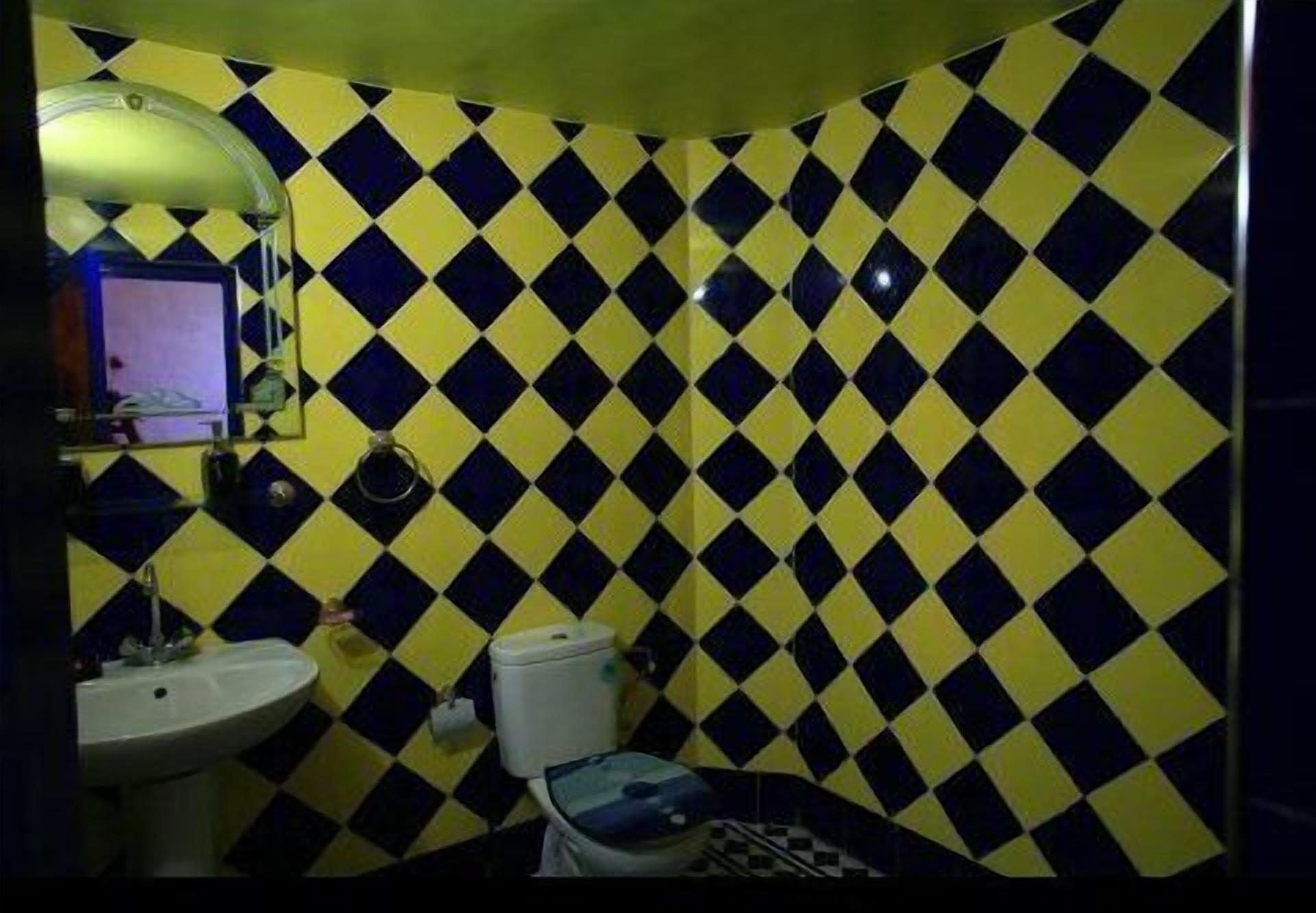 A bathroom with a yellow and black diamond-patterned tile wall, a white sink, and a toilet.