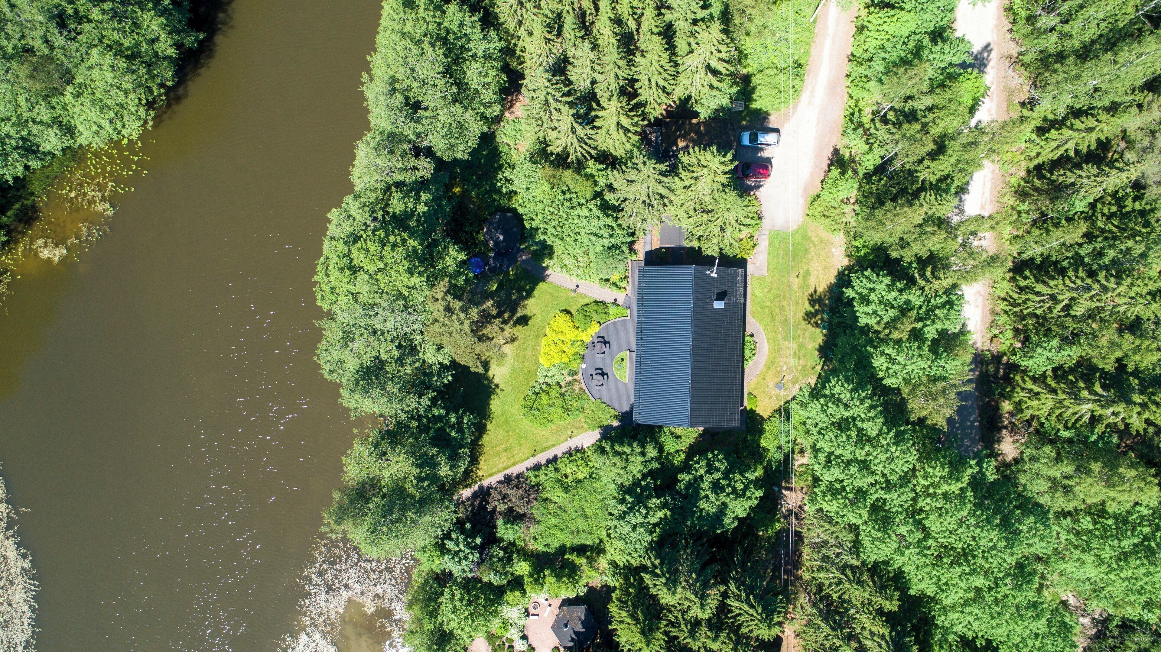 Vista aerea di una casa con un ampio vialetto, immersa in una fitta foresta e bagnata da un fiume.