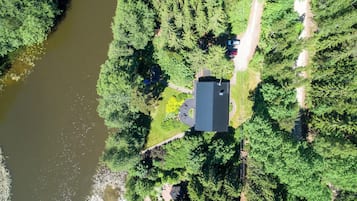 Vista aerea di una casa con un ampio vialetto, immersa in una fitta foresta e bagnata da un fiume.