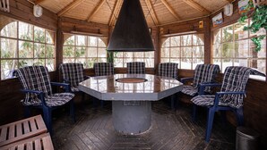 A wooden interior with a central table surrounded by plaid chairs, large windows, and a hanging light fixture. - Villa Struka (Pyhtaa)