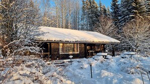 A wooden cabin with a snow-covered roof, surrounded by snow-laden trees and bushes. - Villa Struka (Pyhtaa)