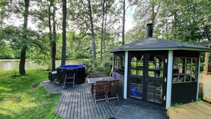 A wooden deck with a hot tub, a covered seating area, and a view of a lake surrounded by trees.