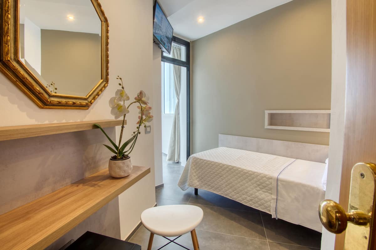 A bedroom with a bed, a bedside table, a chair, a mirror, and a potted orchid.