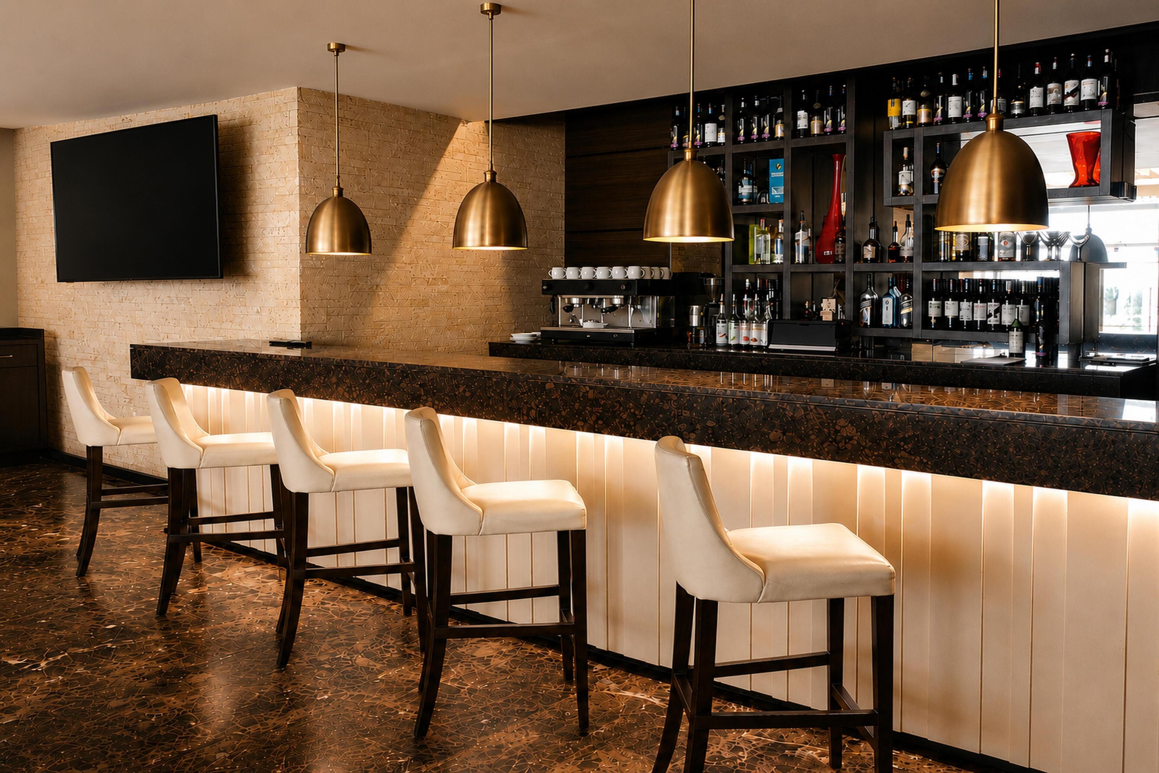 A bar area with a long counter, multiple bar stools, and a variety of bottles and glasses on shelves.