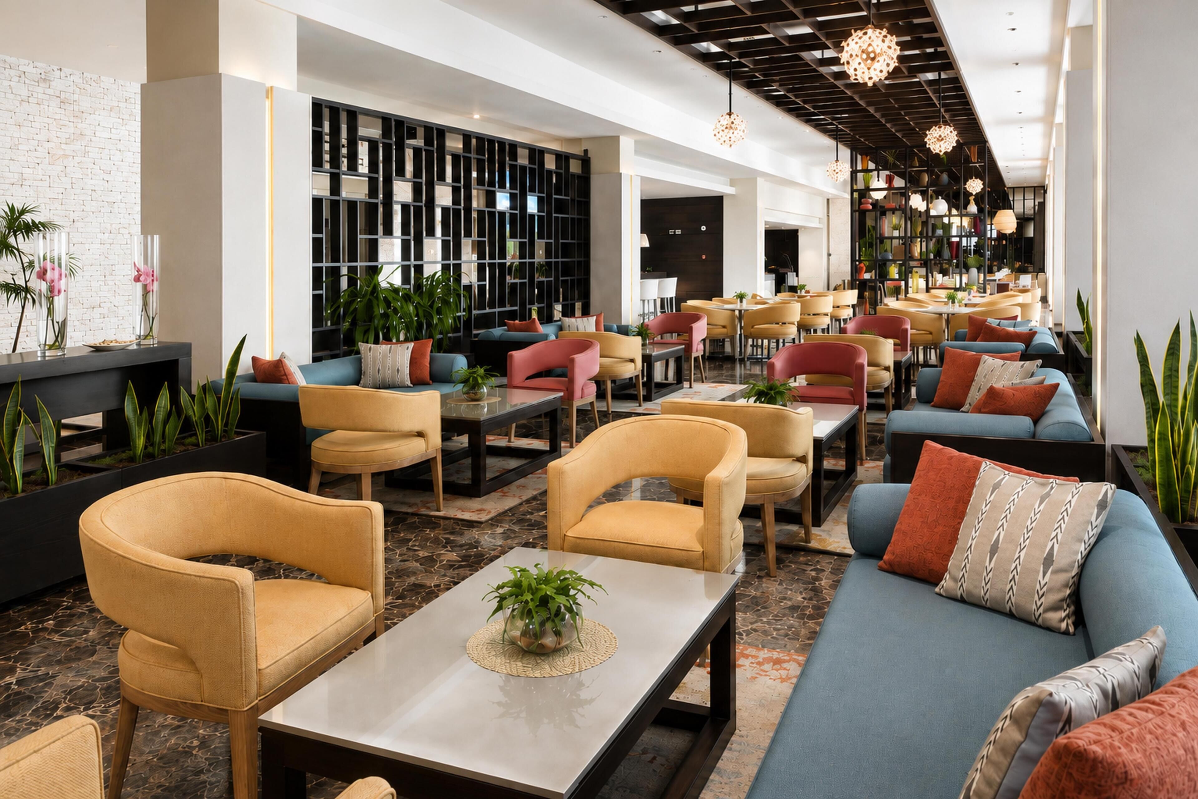 En moderne hotellobby med siddeområder, en reol og dekorative planter.