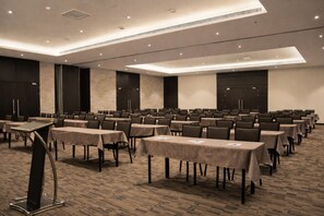 Un salón de conferencias con varias mesas y sillas, un atril y piso alfombrado.