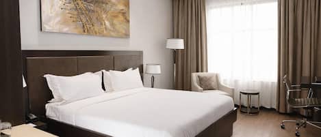 Habitación de hotel con una cama grande, un escritorio, una silla, una lámpara y un cuadro en la pared.
